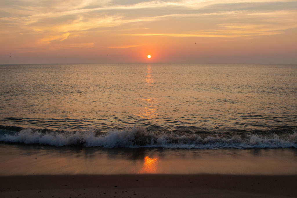 Pink and orange sunrise over the water at Nauset Beach with small waves lapping the shore