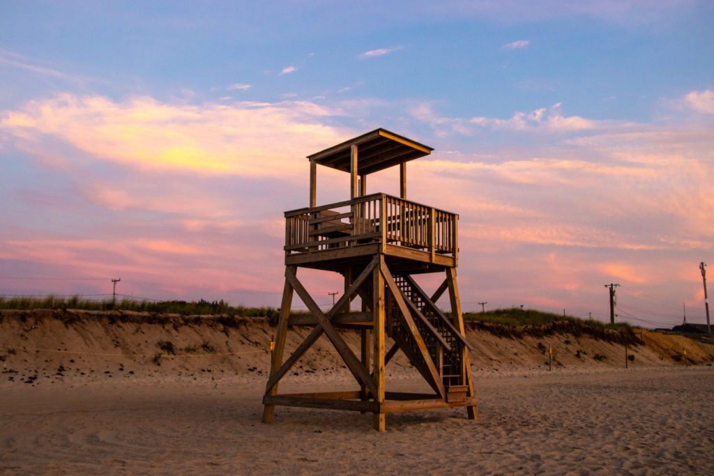 A lighthouse on Nauset Beach during sunrise with a pink sky in the background