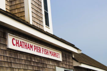 Chatham Fish Pier Market sign on the top of the building with blue sky in the background | Brewster By the Sea Cape Cod Inn | Brewster, MA