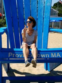 Brown haired woman sitting in an oversized bright blue rocking chair on a sandy beach | Brewster By the Sea Cape Cod Inn | Brewster, MA